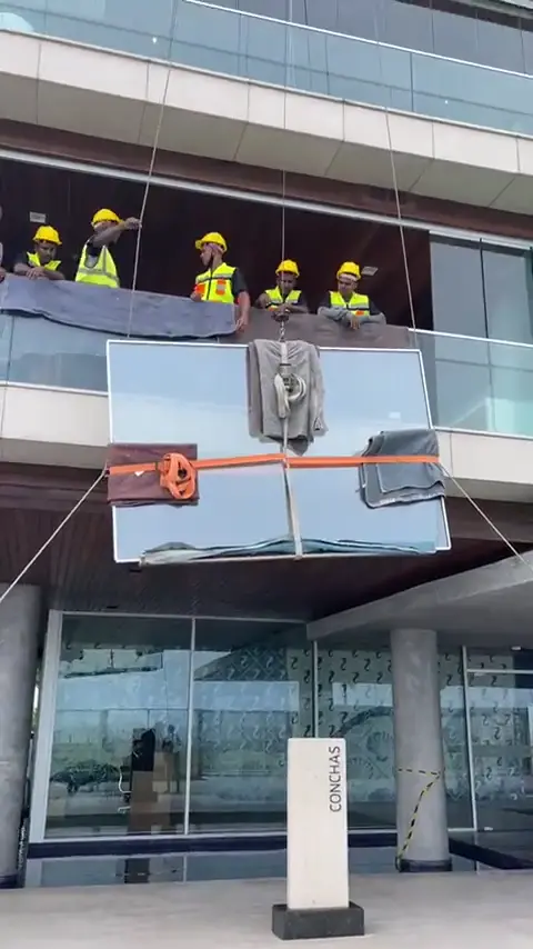 Equipe com capacetes içando material em fachada de vidro